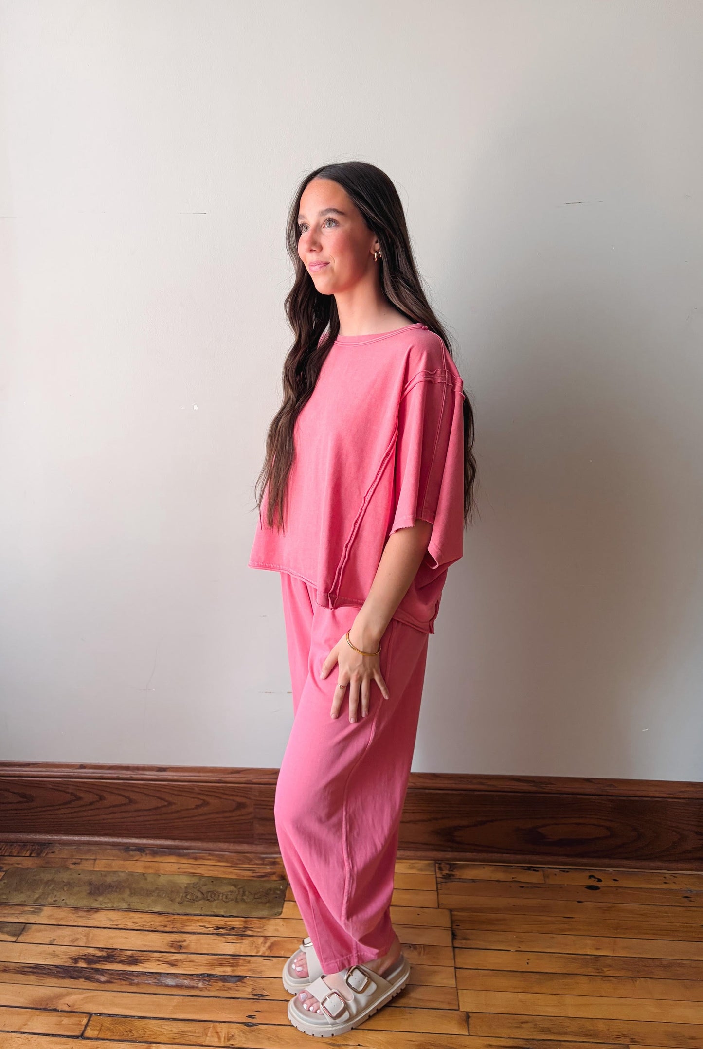 Woman wearing a pink outfit standing against a white wall.
