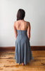Woman wearing a blue dress standing on a wooden floor with a white wall background