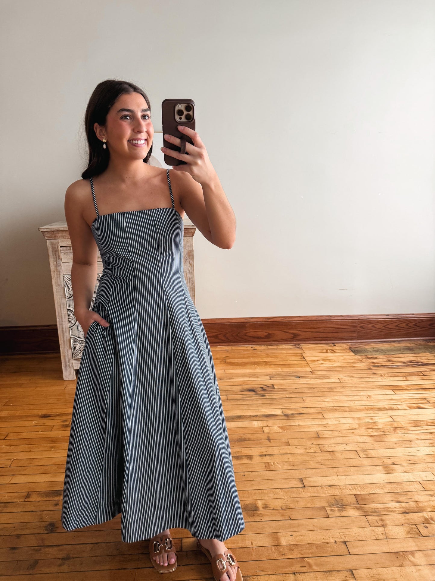Woman taking a mirror selfie wearing a blue striped dress in a room with wooden flooring.