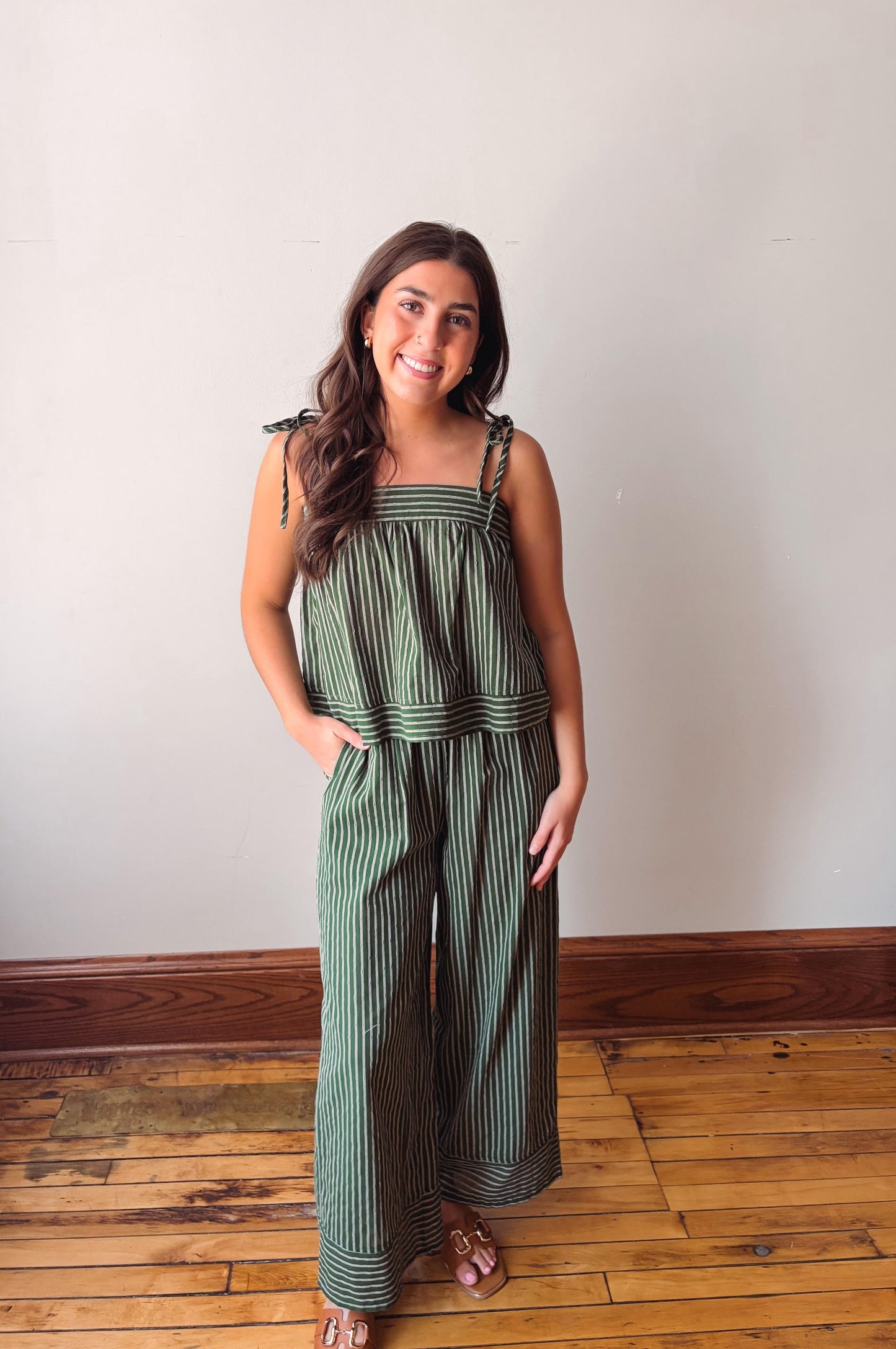 Woman wearing a green striped jumpsuit standing on a wooden floor with a white wall background