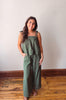 Woman wearing a green striped jumpsuit standing on a wooden floor with a white wall background