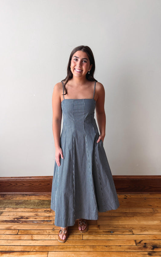 Woman wearing a blue dress standing on a wooden floor with a white wall background