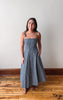 Woman wearing a blue dress standing on a wooden floor with a white wall background