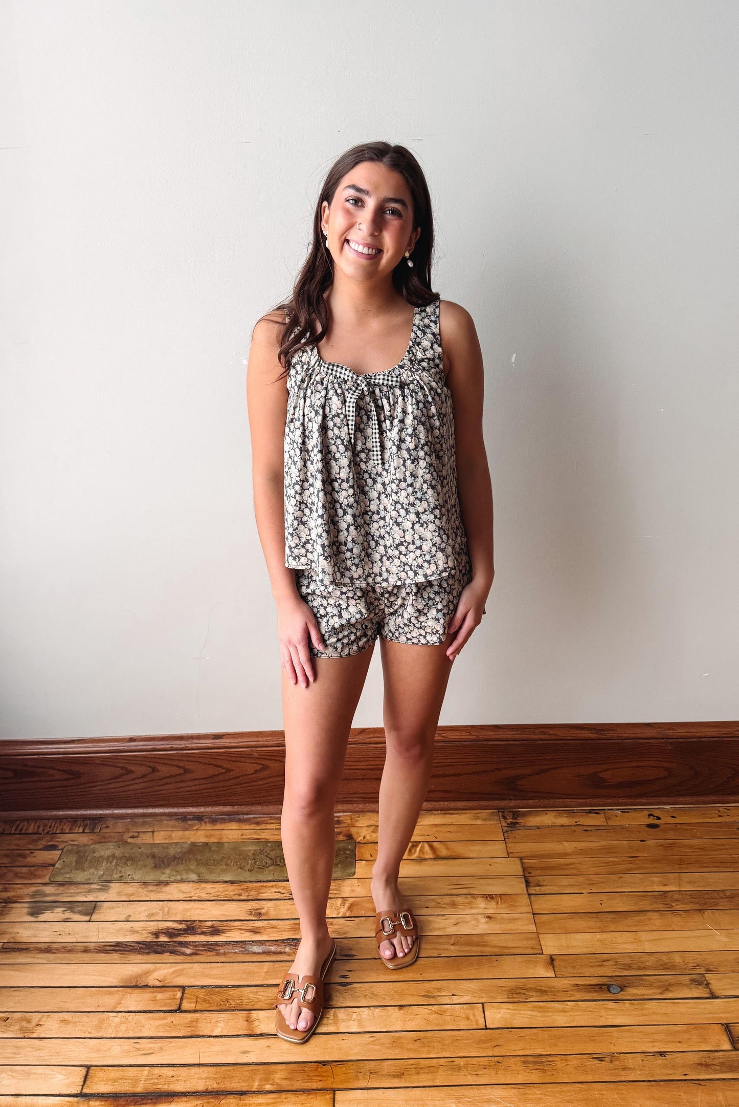 Woman wearing a patterned romper standing on a wooden floor with a white wall background
