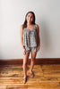 Woman wearing a patterned romper standing on a wooden floor with a white wall background
