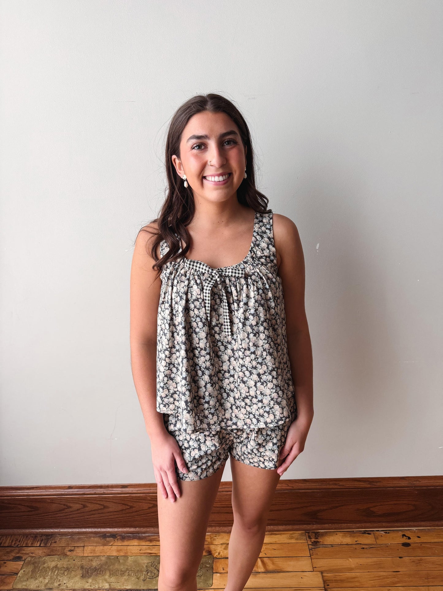 Woman wearing a floral romper against a plain wall.