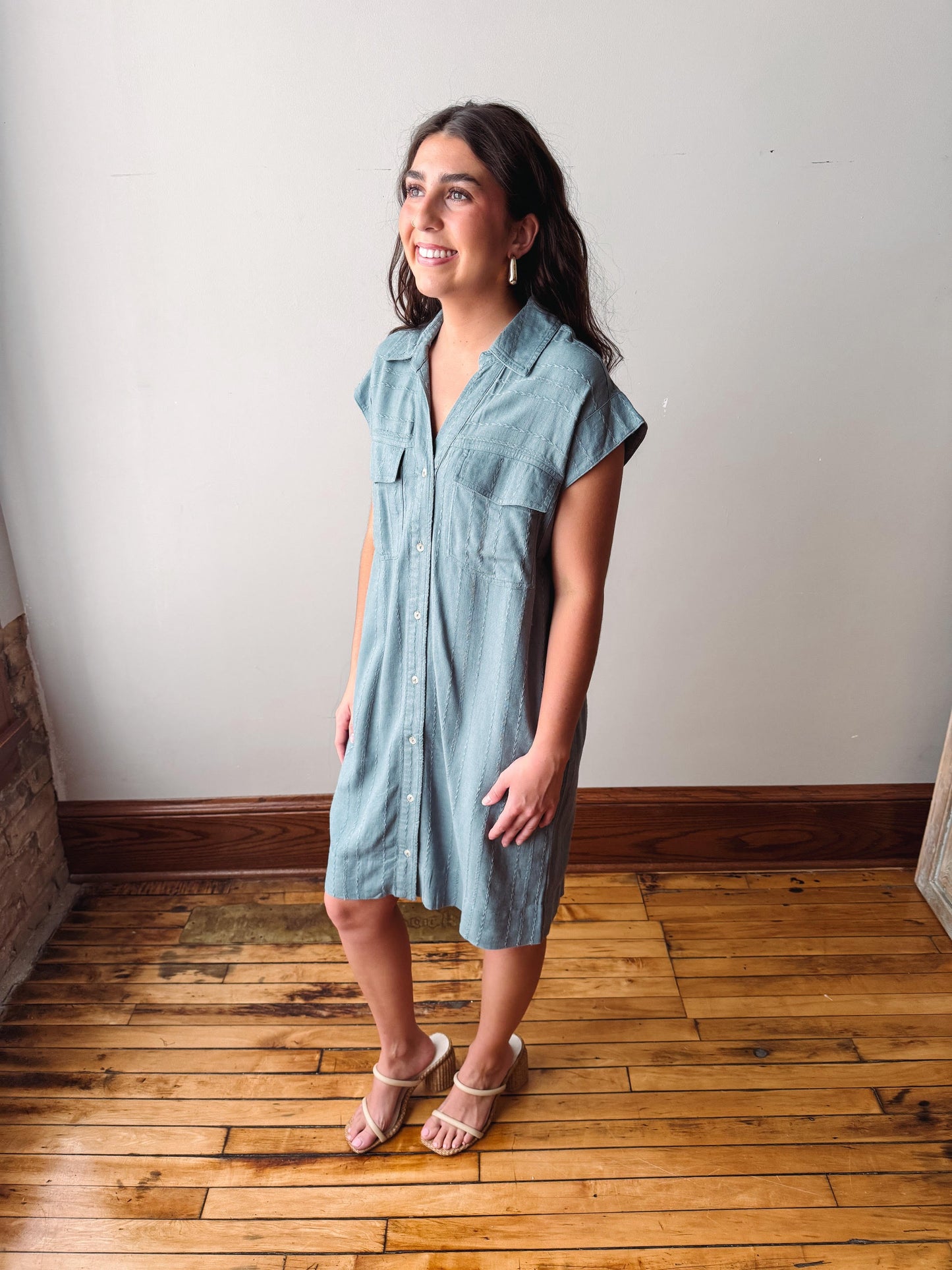 Woman wearing a light blue dress standing on a wooden floor with a white wall background