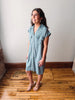 Woman wearing a light blue dress standing on a wooden floor with a white wall background