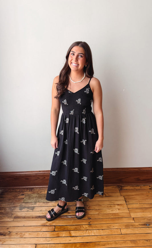 Woman wearing a black dress with white patterns on a wooden floor.