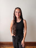 Woman wearing a black sleeveless top and black pants against a plain wall.