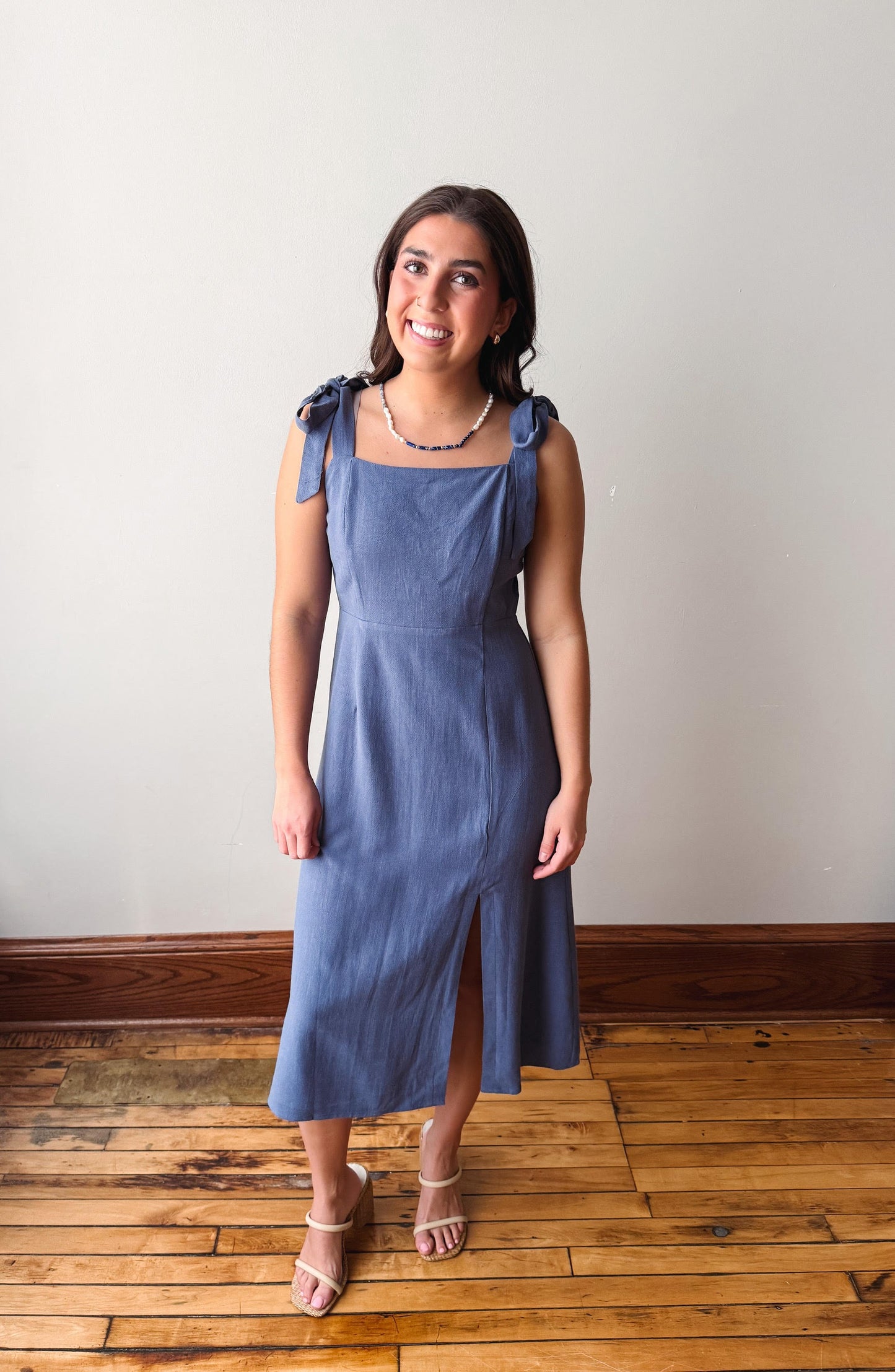 Woman wearing a blue dress standing on a wooden floor with a white wall background