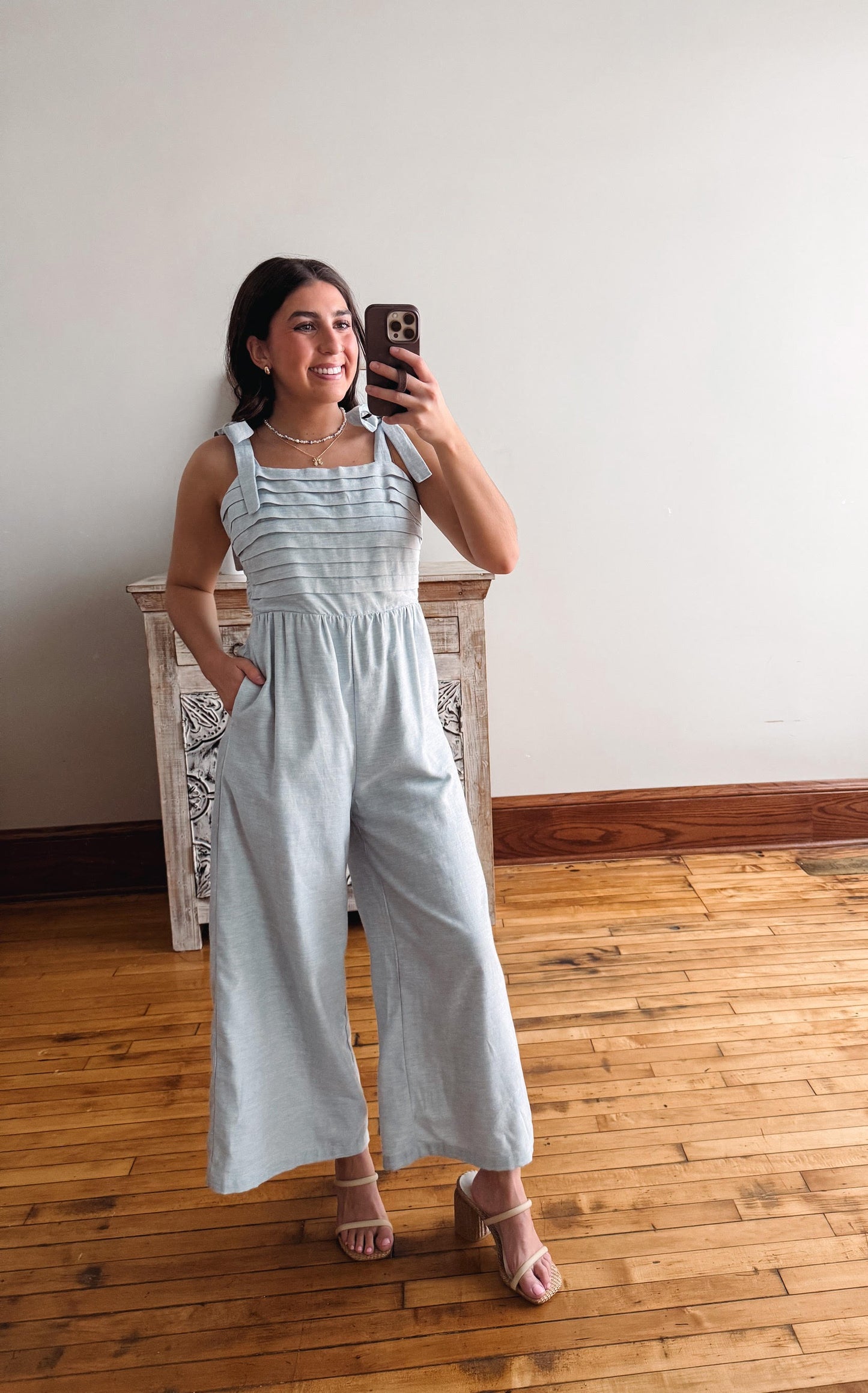 Woman wearing a light blue striped jumpsuit taking a mirror selfie.