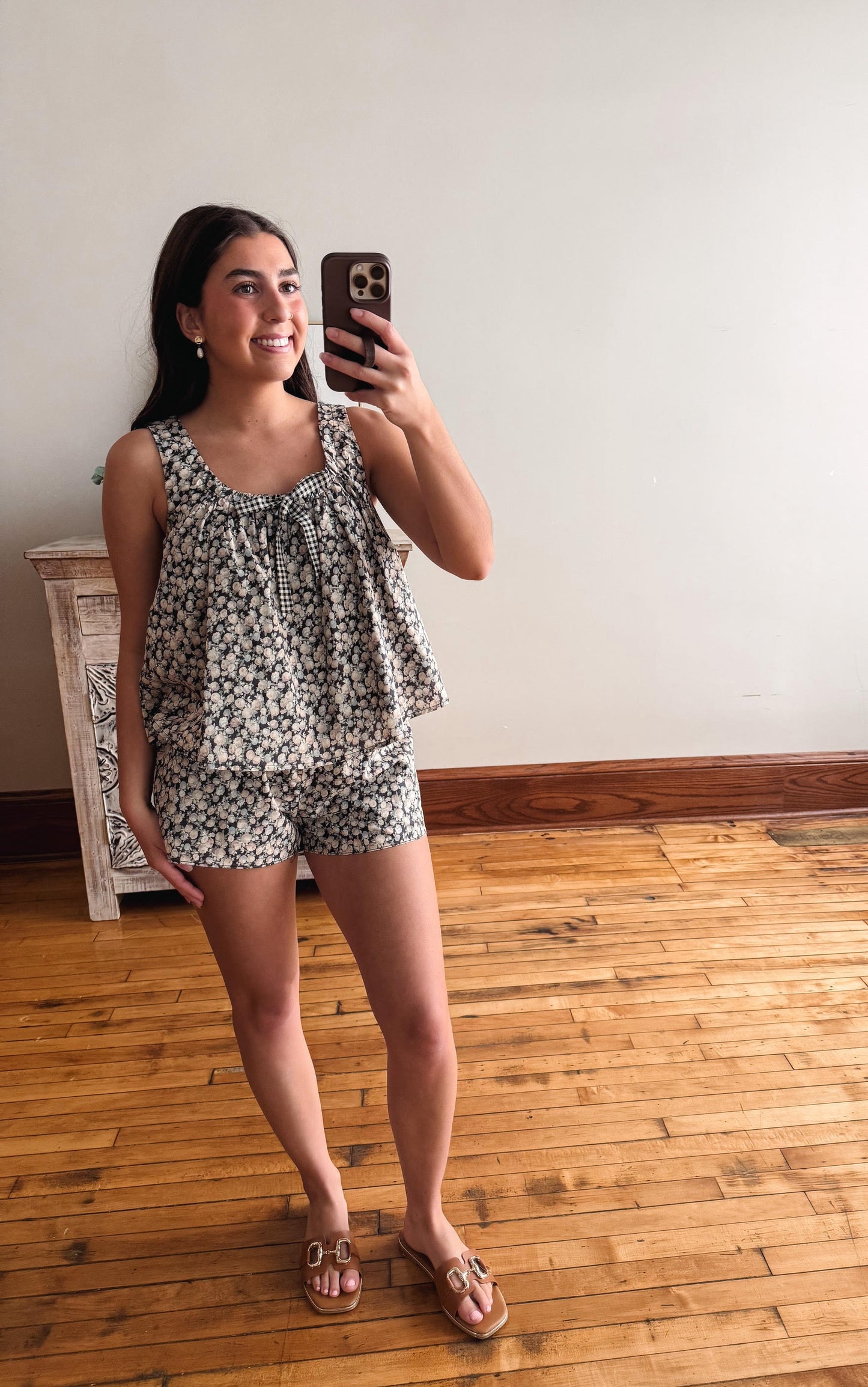 Woman taking a mirror selfie wearing a floral romper in a room with wooden flooring.