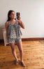 Woman taking a mirror selfie wearing a floral romper in a room with wooden flooring.