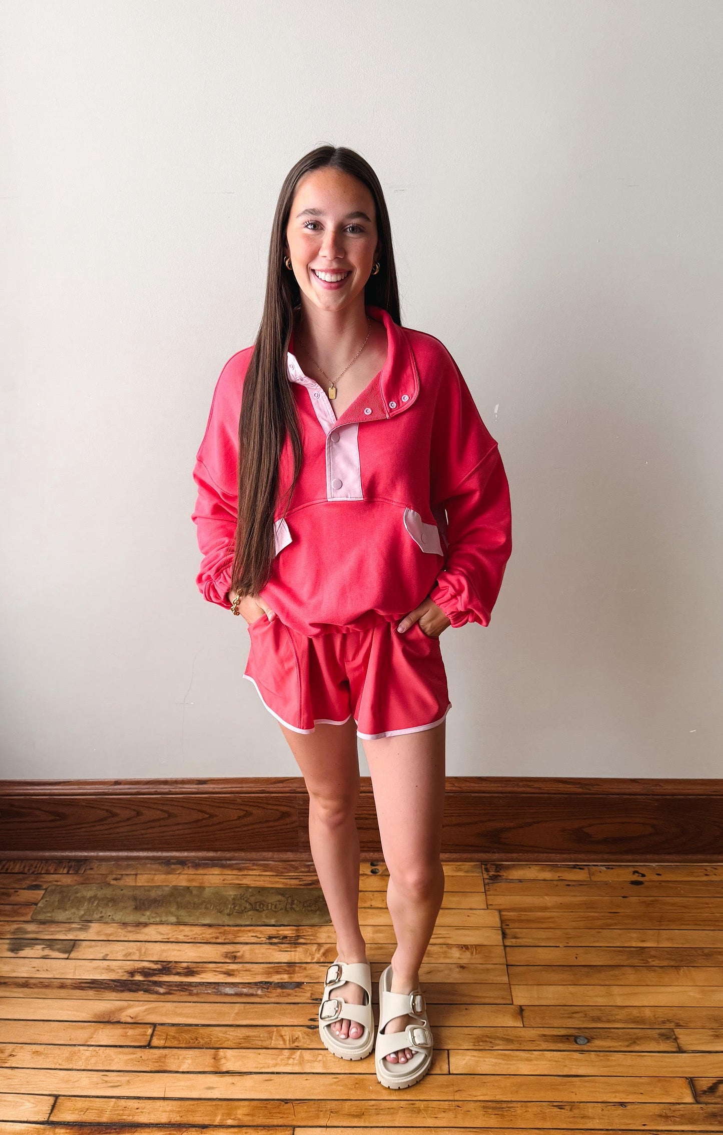 Woman wearing a pink outfit standing on a wooden floor with a white wall background