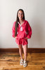 Woman wearing a pink outfit standing on a wooden floor with a white wall background