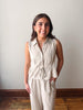 Woman wearing a beige sleeveless top and pants against a plain wall.