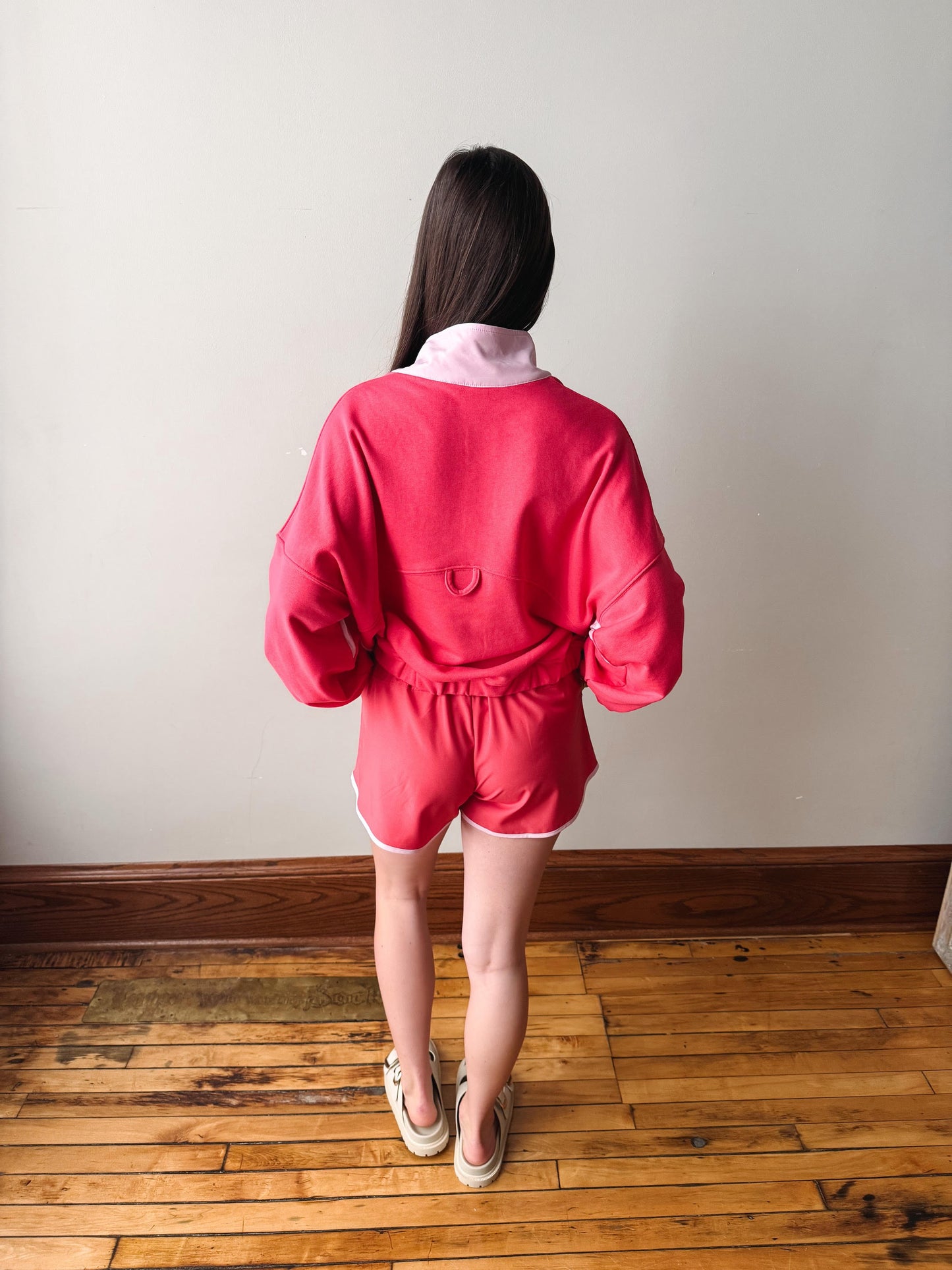 Person wearing a bright pink outfit standing on a wooden floor with a plain wall background