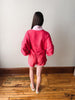 Person wearing a bright pink outfit standing on a wooden floor with a plain wall background