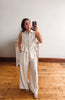 Woman taking a mirror selfie wearing a beige sleeveless top and wide-leg pants in a room with wooden flooring.