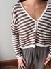 A person wearing a brown and off-white horizontally striped knit cardigan with a V-neck and button-front closure, paired with gray drawstring pants.