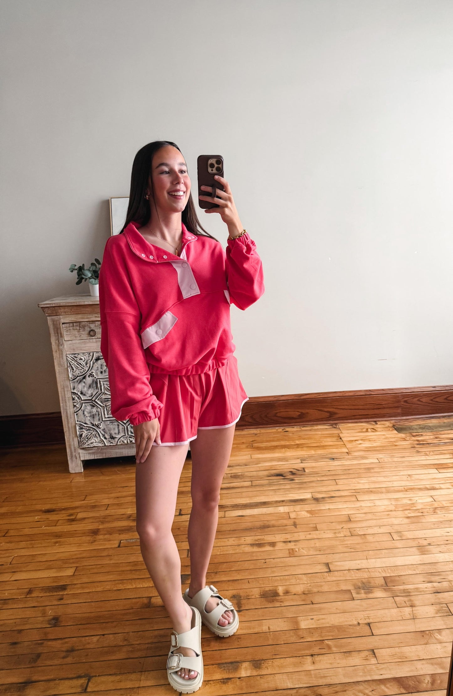 Person taking a mirror selfie wearing a pink outfit in a room with wooden flooring.