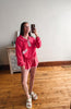Person taking a mirror selfie wearing a pink outfit in a room with wooden flooring.