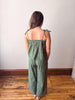 Woman wearing a green striped jumpsuit standing on a wooden floor with a white wall background