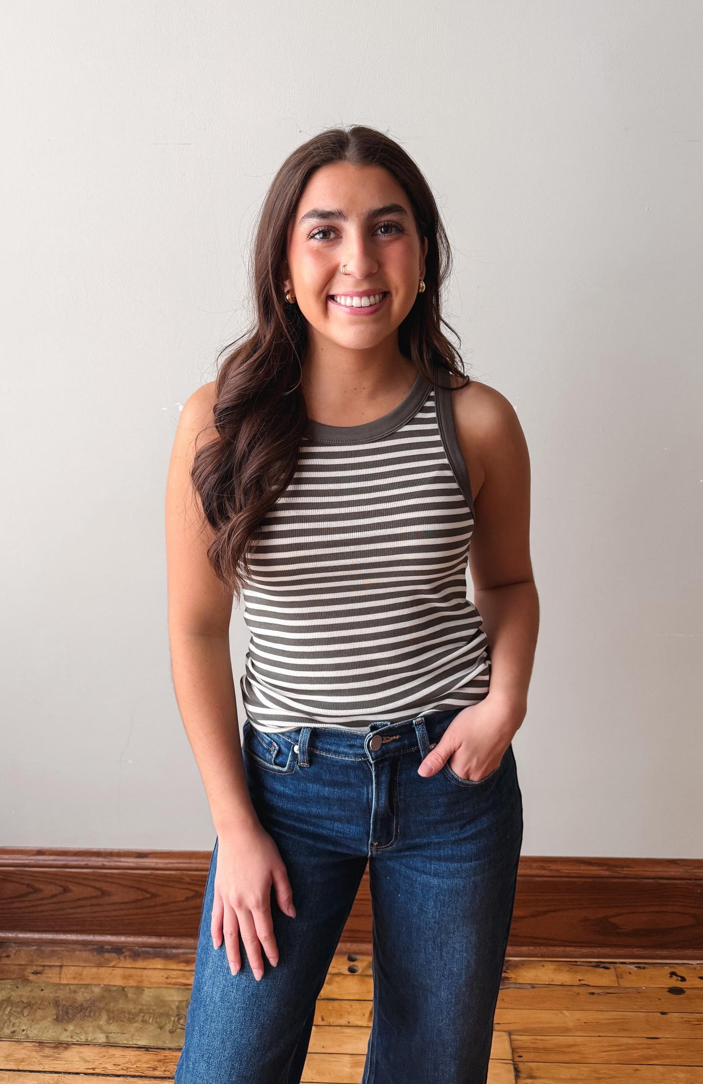 Woman wearing a striped tank top and jeans standing against a plain background