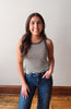 Woman wearing a striped tank top and jeans standing against a plain background