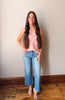 Woman wearing a pink top and blue jeans standing against a plain wall.