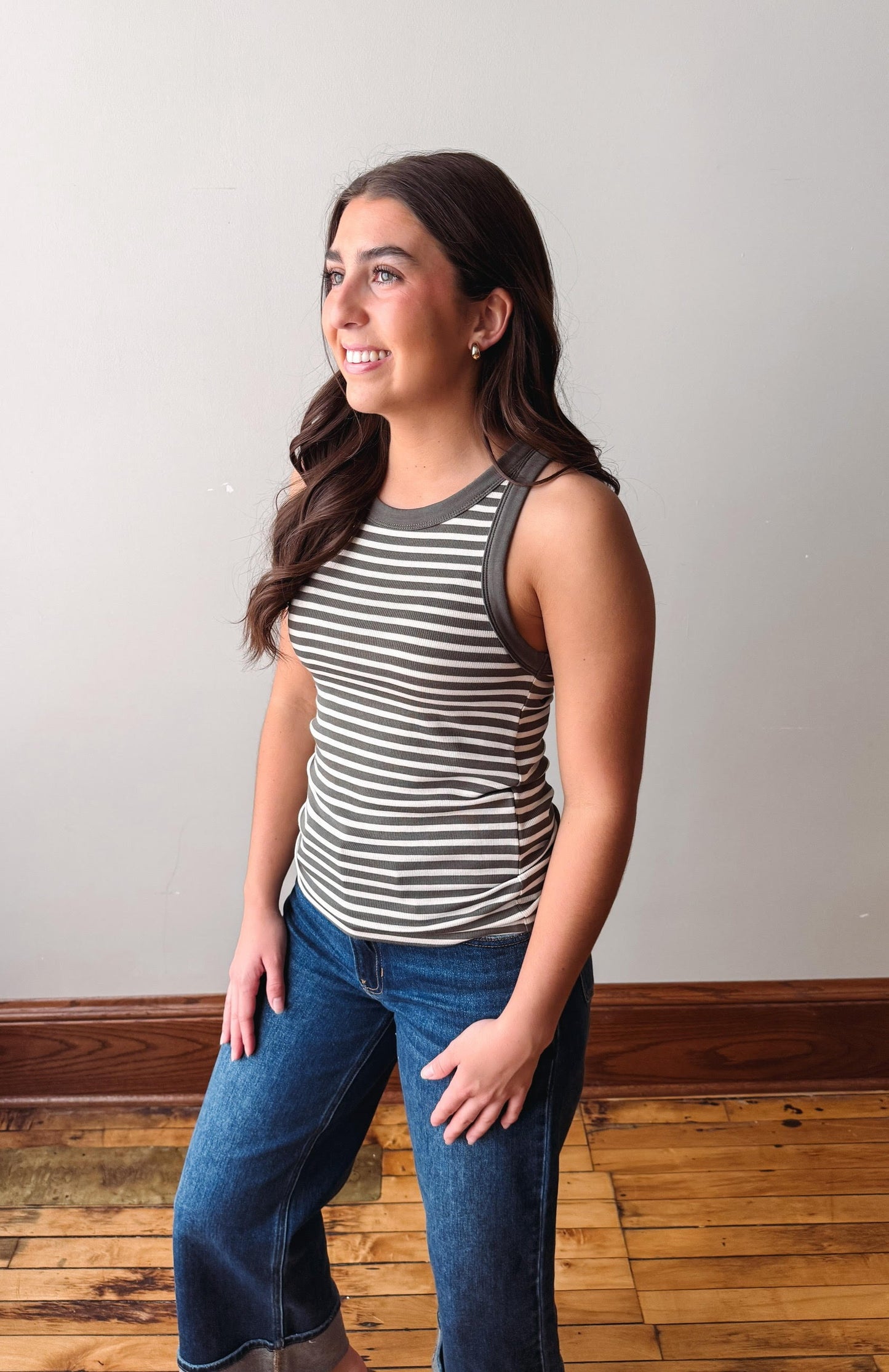 Woman wearing a striped tank top and jeans standing against a plain wall.
