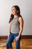 Woman wearing a striped tank top and jeans standing against a plain wall.