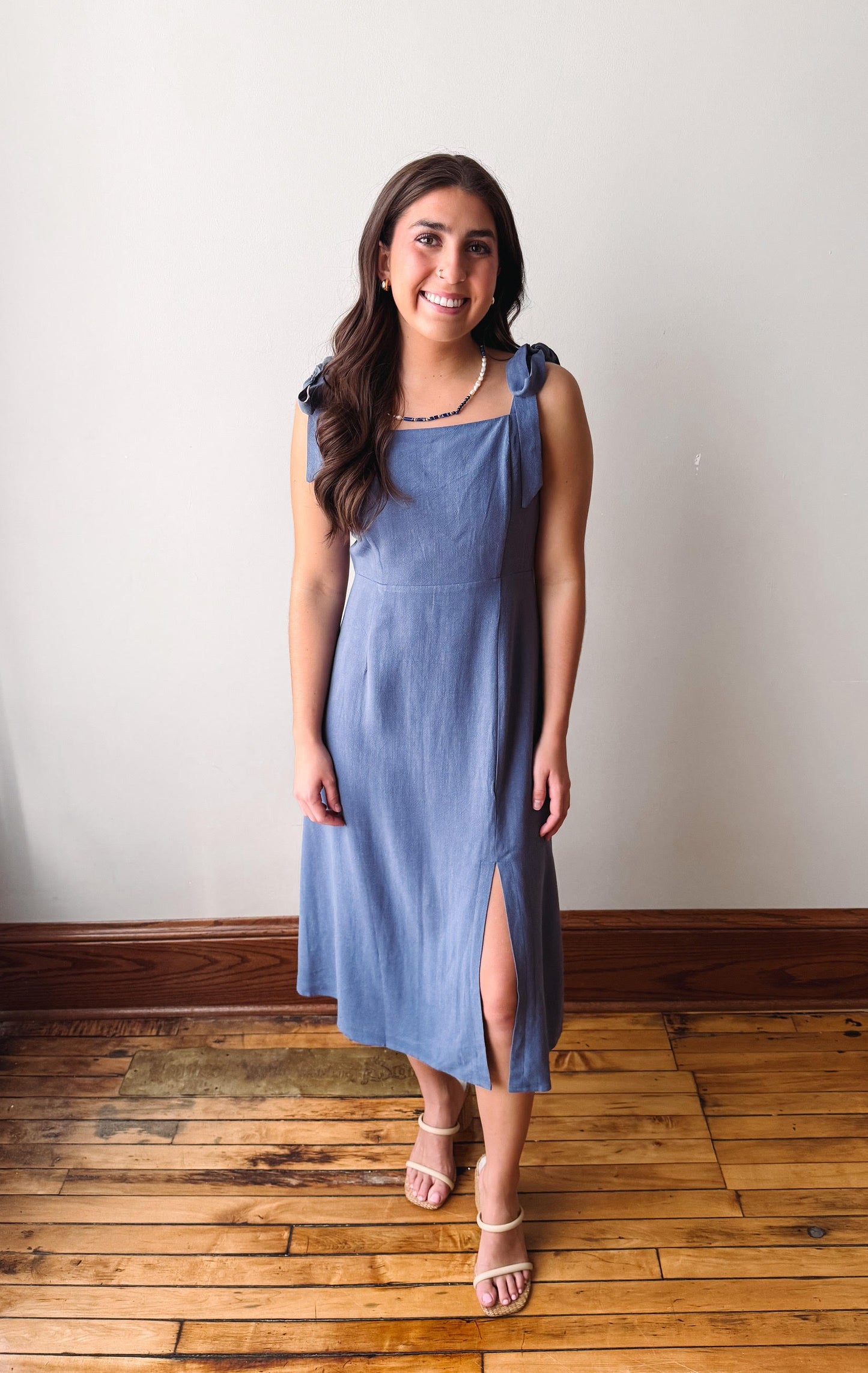 Woman wearing a blue dress standing on a wooden floor with a white wall background