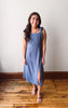 Woman wearing a blue dress standing on a wooden floor with a white wall background