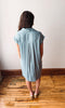 Woman wearing a light blue dress standing on a wooden floor with a white wall background