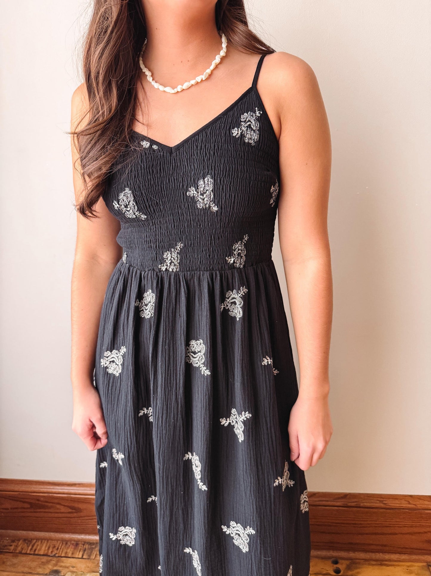 Woman wearing a black dress with white floral patterns against a plain background