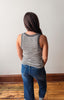 Person wearing a striped tank top and jeans standing against a plain wall.