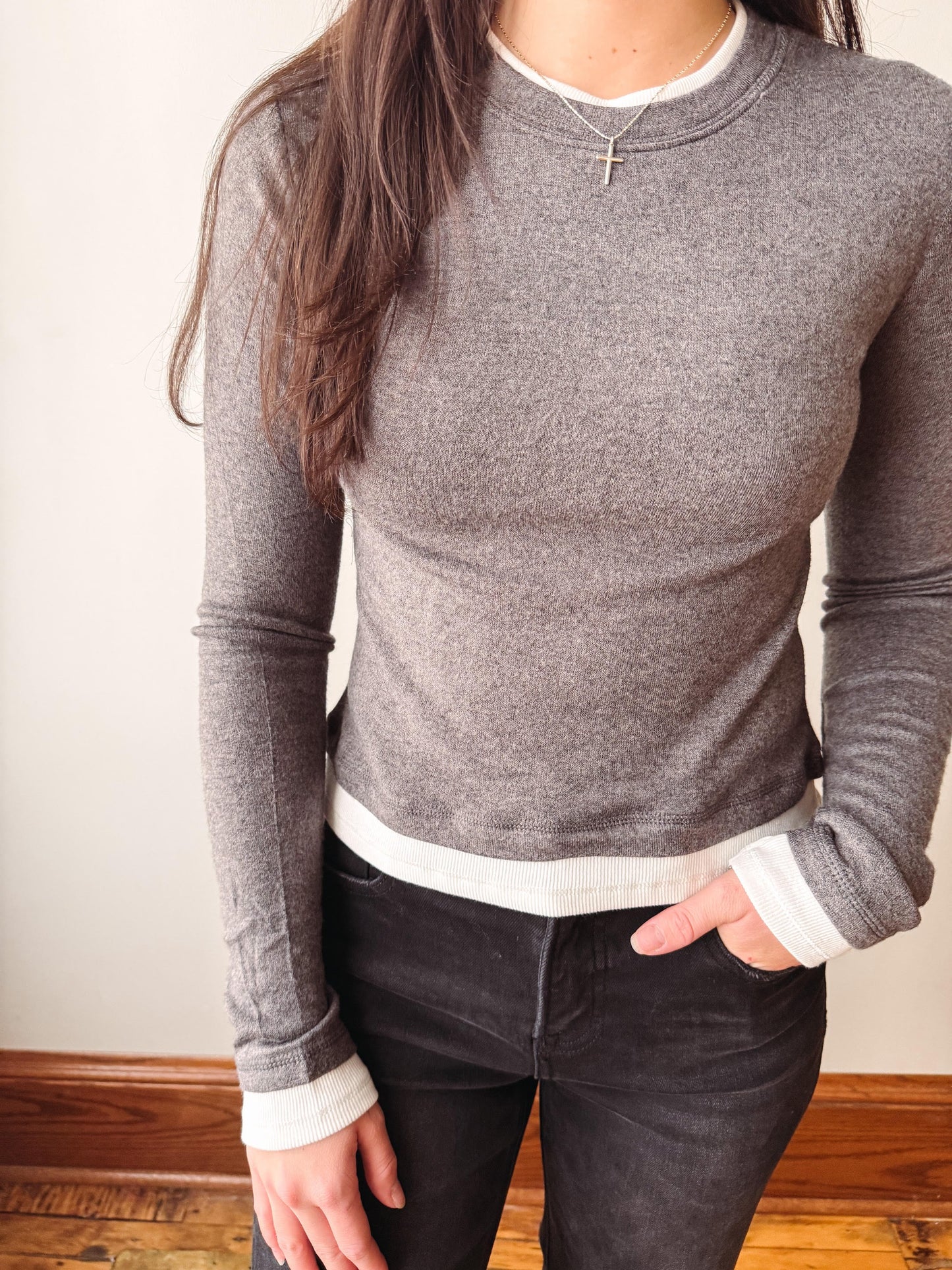A woman wearing a fitted heather gray long-sleeve crewneck sweater with a white ribbed hem and white ribbed cuffs, paired with dark jeans.