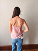 Woman wearing a pink tank top and blue jeans standing against a plain wall.
