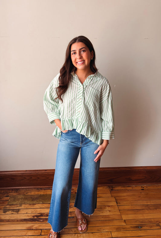 Woman wearing a green striped shirt and blue jeans standing on a wooden floor.