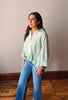 Woman wearing a green striped shirt and blue jeans standing against a plain wall.