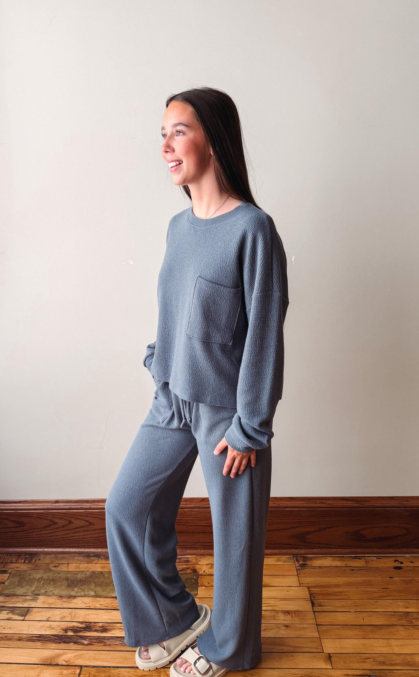Woman wearing a blue outfit standing on a wooden floor against a white wall
