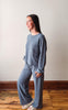 Woman wearing a blue outfit standing on a wooden floor against a white wall
