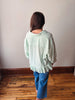 Person wearing a light green striped shirt and blue pants standing on a wooden floor.