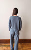 Person wearing a gray sweater and pants standing against a plain wall.