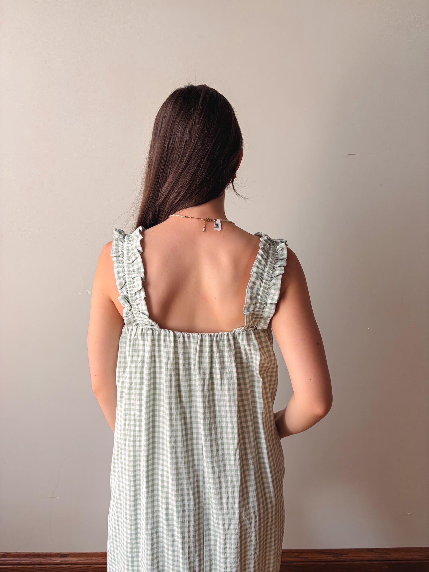 Woman wearing a green checkered dress with ruffled straps against a plain background