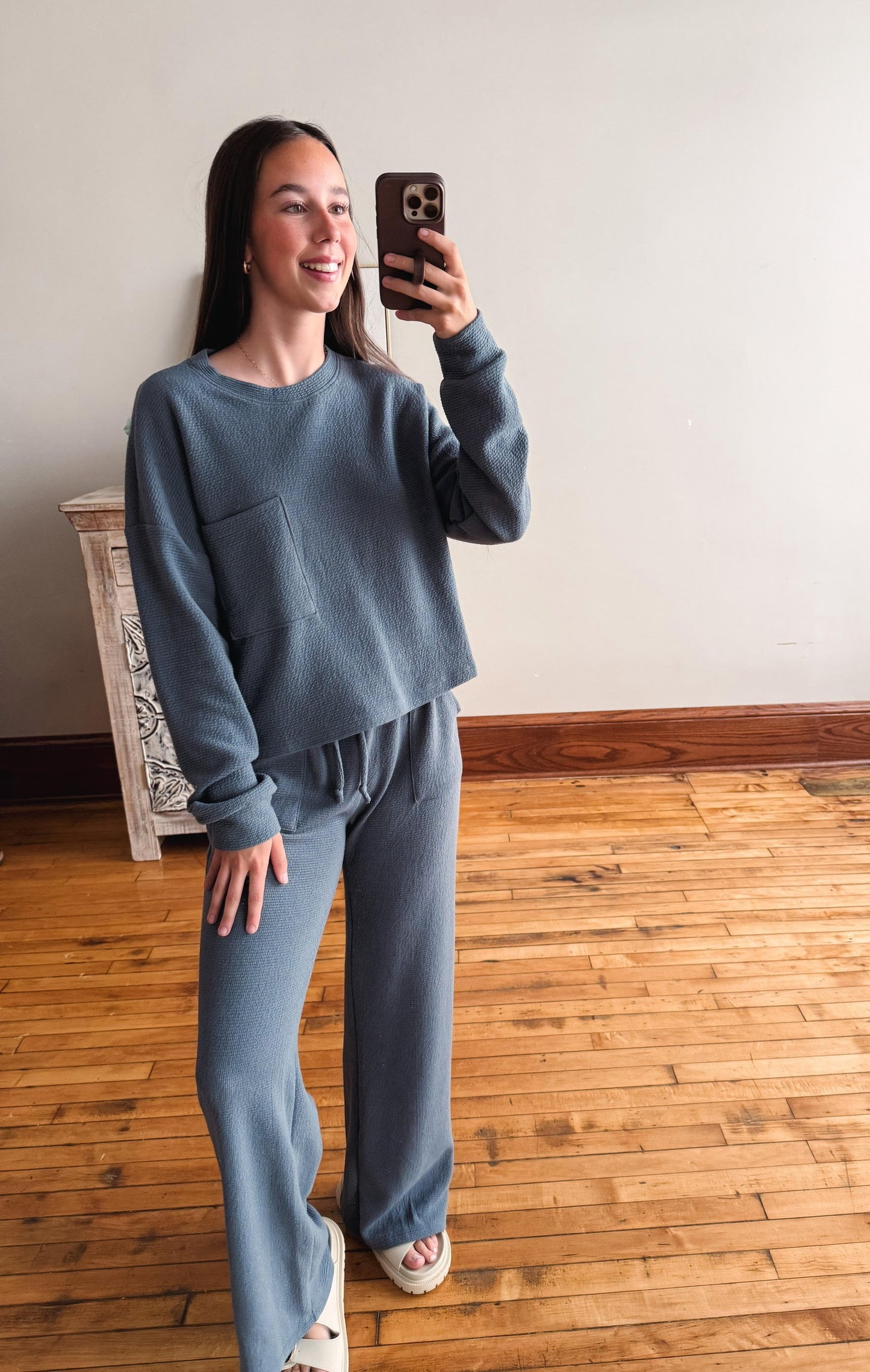 Person wearing a blue outfit taking a mirror selfie on a wooden floor.