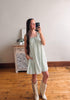 Woman taking a mirror selfie wearing a green checkered dress and white boots in a room with wooden flooring.