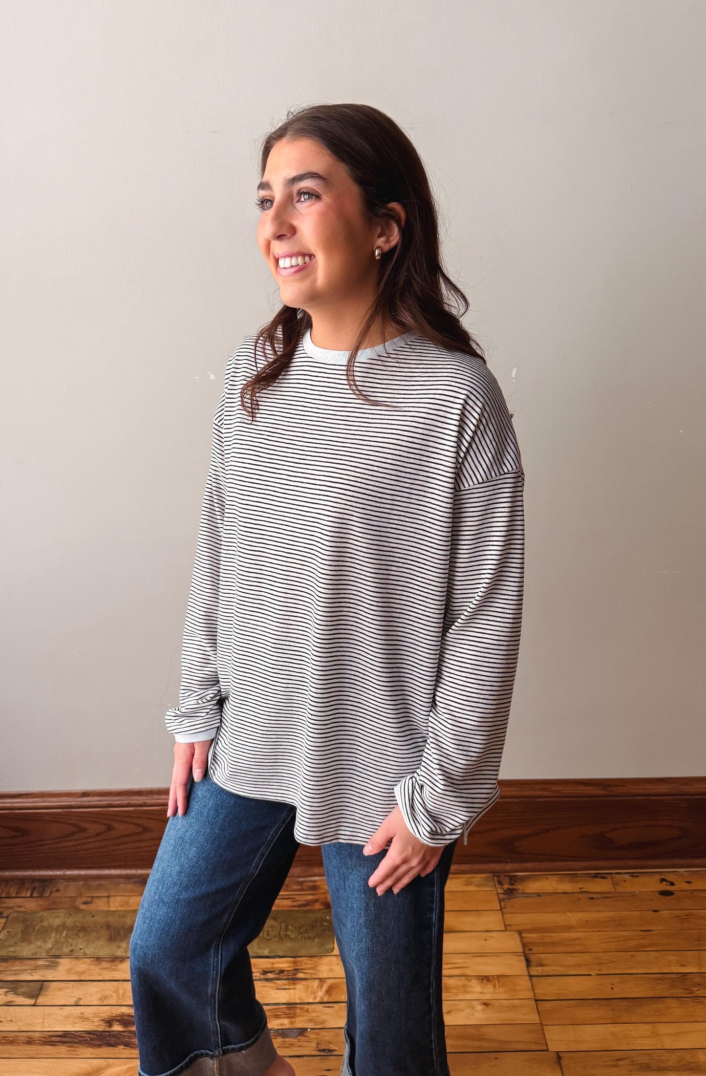 Woman wearing a striped long-sleeve shirt and jeans standing on a wooden floor.